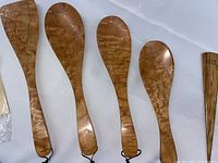 Five olive wood serving utensils laid flat showing size variation and hanging loops