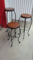 Three wooden and metal framed plant stands with mahogany stain on the tops, placed together on a concrete floor.