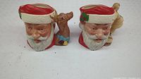 Two Royal Doulton decorative Santa Claus Christmas mugs side by side showing front faces and reindeer figures.