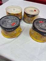 Four spindles of Sony DVD-R discs with yellow and black packaging on white surface. Three sealed spindles and one open.