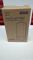 Front view of sealed cardboard box showing product name HappyLight 6000, model VT05FWW1, and Verilux branding in blue ink on brown box.