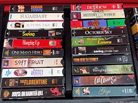 Close-up photo of one storage container filled with 18 visible VHS movie jackets. Titles visible include Sugar Town, Sugar Baby, Autumn Tale, Swing, Hanging Up, One Man's Hero, Soft Fruit, Paperback Romance, The Florentine, House on Haunted Hill on VHS tapes.