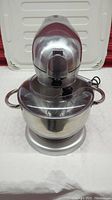 Front view of stainless steel stand mixer with attached splash guard and mixing bowl on table.