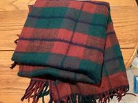 Green and red tartan throw folded on wooden floor showing fringed edges.