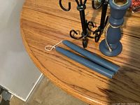 Two blue taper candles lying flat on a wooden table with a blue wooden single candlestick holder and black metal 3-arm candle holder in the background.