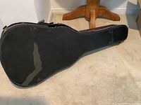 Photo of a black soft guitar carrying case on carpeted floor showing wear and fading.