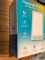 Photo of the lamp box front showing brand Verilux, HappyLight Touch, and main features such as resetting sleep cycle, overcoming fatigue, alleviating winter blues, 10,000 LUX, UV safe, and flicker-free LED light.