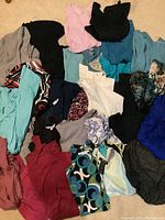 Photo showing a variety of folded long sleeve women's tops in different colors and patterns spread on a carpeted floor.