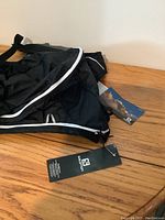 Front view of new black Salomon backpack with brand tag showing, placed against plain background.