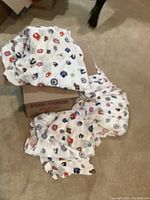 Two Canadian hockey team twin bedding sets including fitted and top sheets spread and partially folded on tan carpet near a cardboard box.