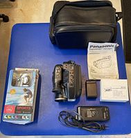Full lot including camcorder, carrying case, charger, battery, manual, sports cam and accessories displayed on blue surface.