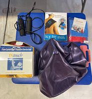 Fitness lot items arranged on a blue padded bench, including a deflated purple exercise ball, a boxed Crystal Edge Premium Exercise Ball, a black-handled jump rope, multicolored resistance bands in plastic packaging, small pink dumbbell weight, and Ice It shoulder cold wrap box.