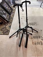 Three black metal guitar stands grouped together showing tripod base and padded neck supports on a concrete floor.