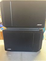 Front view of two black Bose speakers stacked, both with fabric grill and Bose logo bottom right.