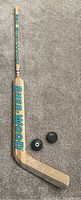 Full view of signed Sher-Wood goalie hockey stick and two NHL hockey pucks on carpeted floor.