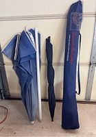 Photo showing all three umbrellas standing upright against a wall, with the Tommy Bahama umbrella in its branded carrying bag, the black Senz umbrella with ergonomic handle, and a smaller plain black umbrella.