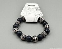 Photo of heavy beaded bracelet with alternating dark grey solid and tan patterned beads on white marble-effect card