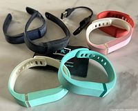 Photo of six Fitbit Flex bracelets in black, navy, white, red, teal, and mint green colors arranged with a black Fitbit Flex USB charge cord and a setup booklet on a flat surface.