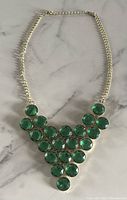 Front view of gold tone chain necklace with large green faceted round stones arranged symmetrically