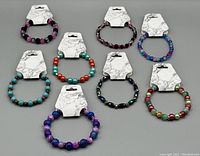 Eight multicolor beaded bracelets arranged in two rows on grey background, each bracelet on a white tag.