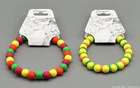 Two neon multicolor beaded bracelets on marble-style card holders, showing bright round matte beads strung on stretchy cord.