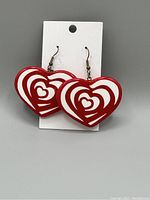 Photo shows a pair of red and white heart-shaped dangle earrings with metal hooks on a white card.