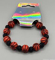 Photo of a beaded stretch bracelet with orange basketball beads alternating with black sparkly beads on a gray background.