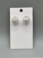 Photo showing a pair of spherical clear globe earrings with snowflake glitter inside mounted on a white display card.