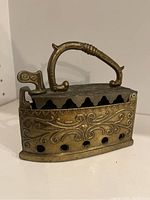 Front view of antique brass incense burner showing embossed pattern, handle, and ventilation holes near base.