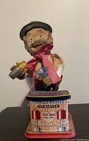 Front view of the lithographed bartender toy showing facial features, cocktail shakers, and vintage litho base.