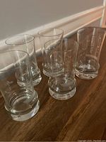 Five clear glass tumblers placed on a table, showing their size, shape, and thick solid bases.