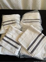 Photo showing multiple packages containing stacks of white cotton wash cloths with two gray stripes.