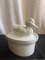 White ceramic duck casserole dish front view showing the duck-shaped handle on the lid.