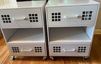 Front view of two white rolling storage carts showing drawers with grid cutout designs and open shelves beneath, with caster wheels visible.
