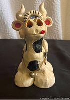 Front view of handmade pottery cow figurine, showing face, horns, eyes, and bell.