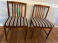 Front-facing view of two wooden chairs with striped cushioned seats showing their vertical slat backs and upholstery pattern.