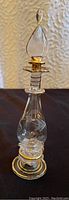 Full view of the vintage miniature perfume bottle with clear glass and gold trim.