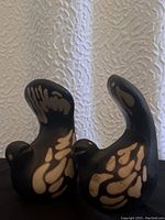 Front and side view of the two black and beige pottery dove birds with raised tails, showing paint details and shape.