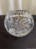 Clear crystal sphere vase showing star and pinwheel cut designs from front view, placed on dark surface with a textured light-colored background.