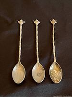 Front view of three miniature sterling silver spoons with teapot tops on handle against a black background
