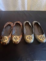Front view of two pairs of Tory Burch flats with gold logo medallions showing leopard print and snakeskin pattern designs.