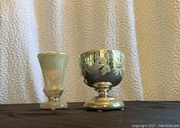 Two vintage mercury glass vessels displayed side by side on black fabric.