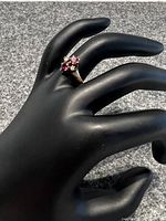 Front-angle view of ring on black display showing two round red garnets and two round white diamonds in yellow gold band