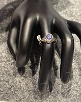 Front‐facing view of ring on black hand form showing tanzanite and bezel setting