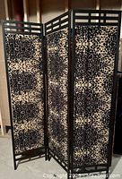 Full view of the three connected folding screen panels covered in textured chenille animal print fabric with hammered wrought mild steel frame corners and lattice work at the top.