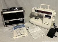 Brother XR-31 sewing machine with included instruction manuals and black tiered hard shell carrying case, all placed on a white surface.