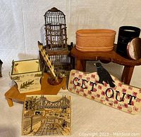 Photo showing assortment of items including wooden birdcage, coral glazed planter, decorative sign, small wooden table, painted tile and feather ornament holder.
