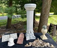 Full set on black cloth outdoors showing plaster pillar, plaster relief tiles, plaster bust, carved stone, wooden scroll, and wooden post cap.