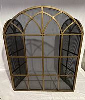 Front view of the large arched fireplace screen with brass-finished iron grid and mesh protection, showing the main panel.