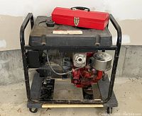 Side angle view of the Generac portable generator showing black frame, red Briggs & Stratton motor, and red metal toolbox on top.